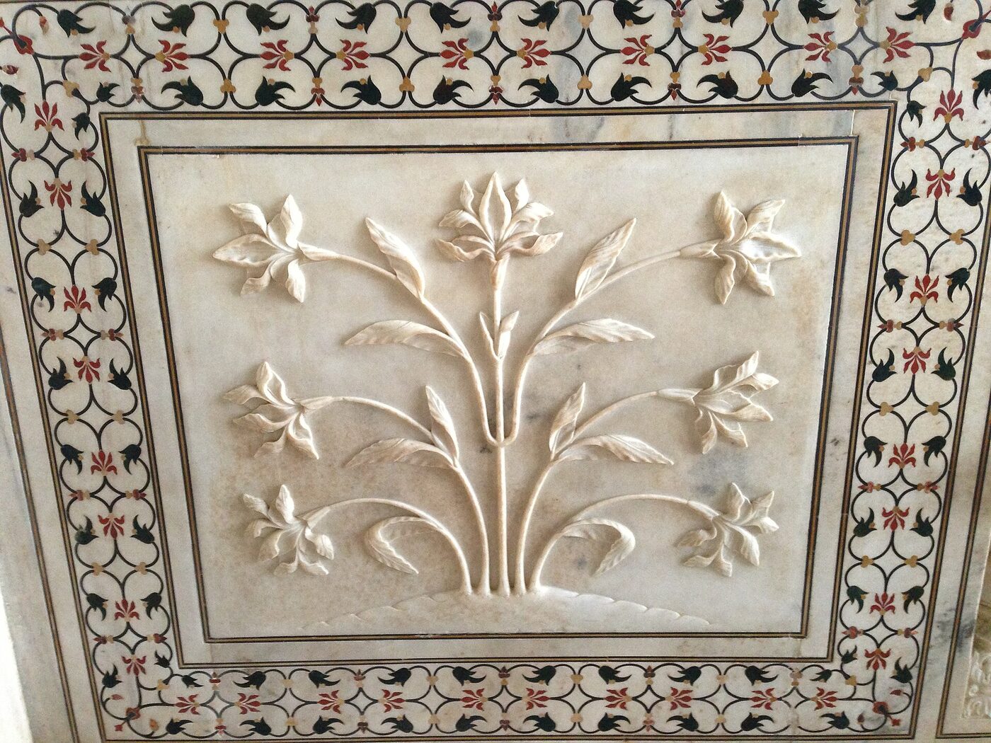 A marble panel inside the Taj Mahal: a carved flower in relief, framed by a border of coloured stones inlaid flush into the white marble