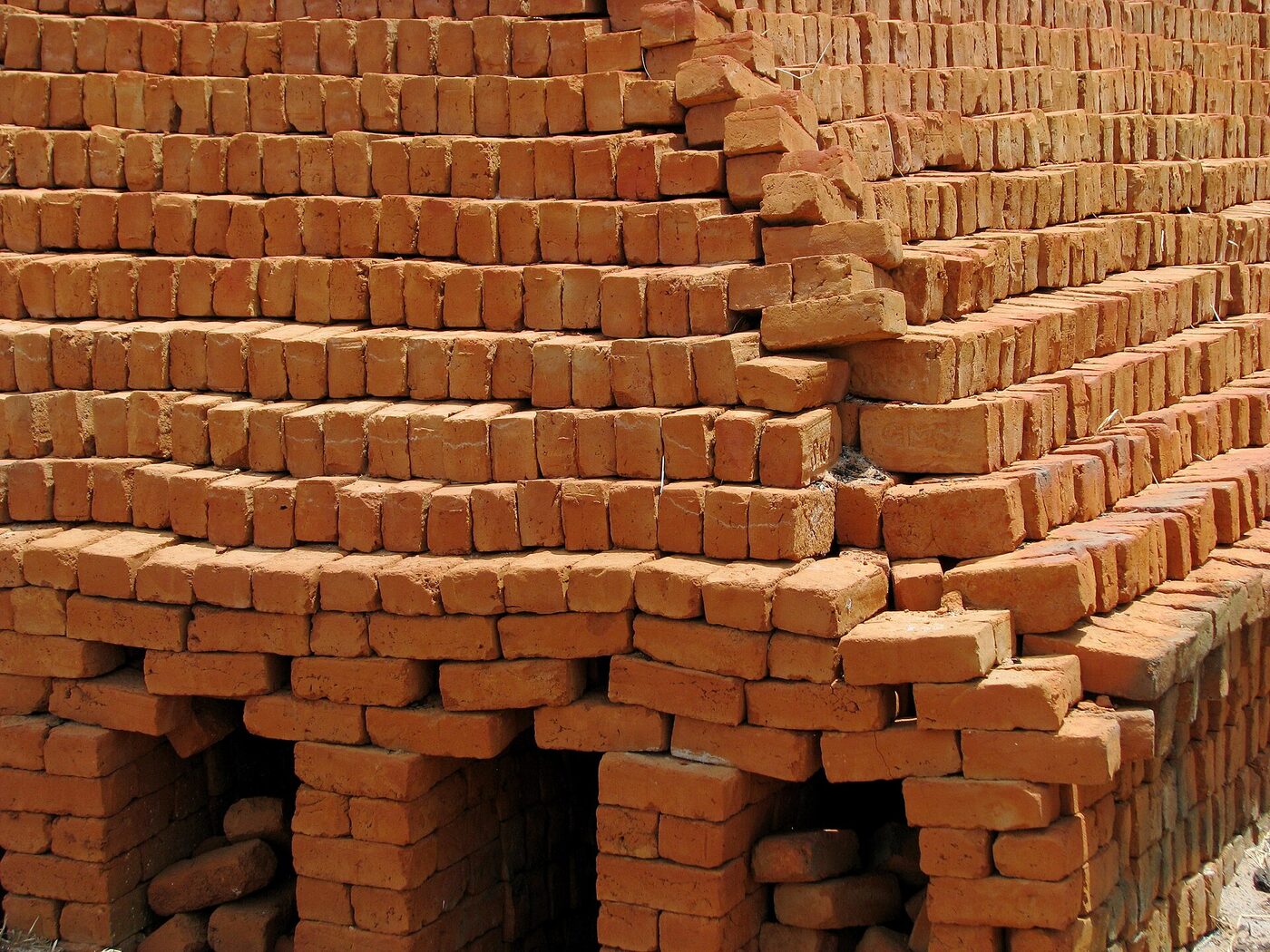 A large field kiln in rural India built entirely from hand-stacked bricks, with firing tunnels visible at the base