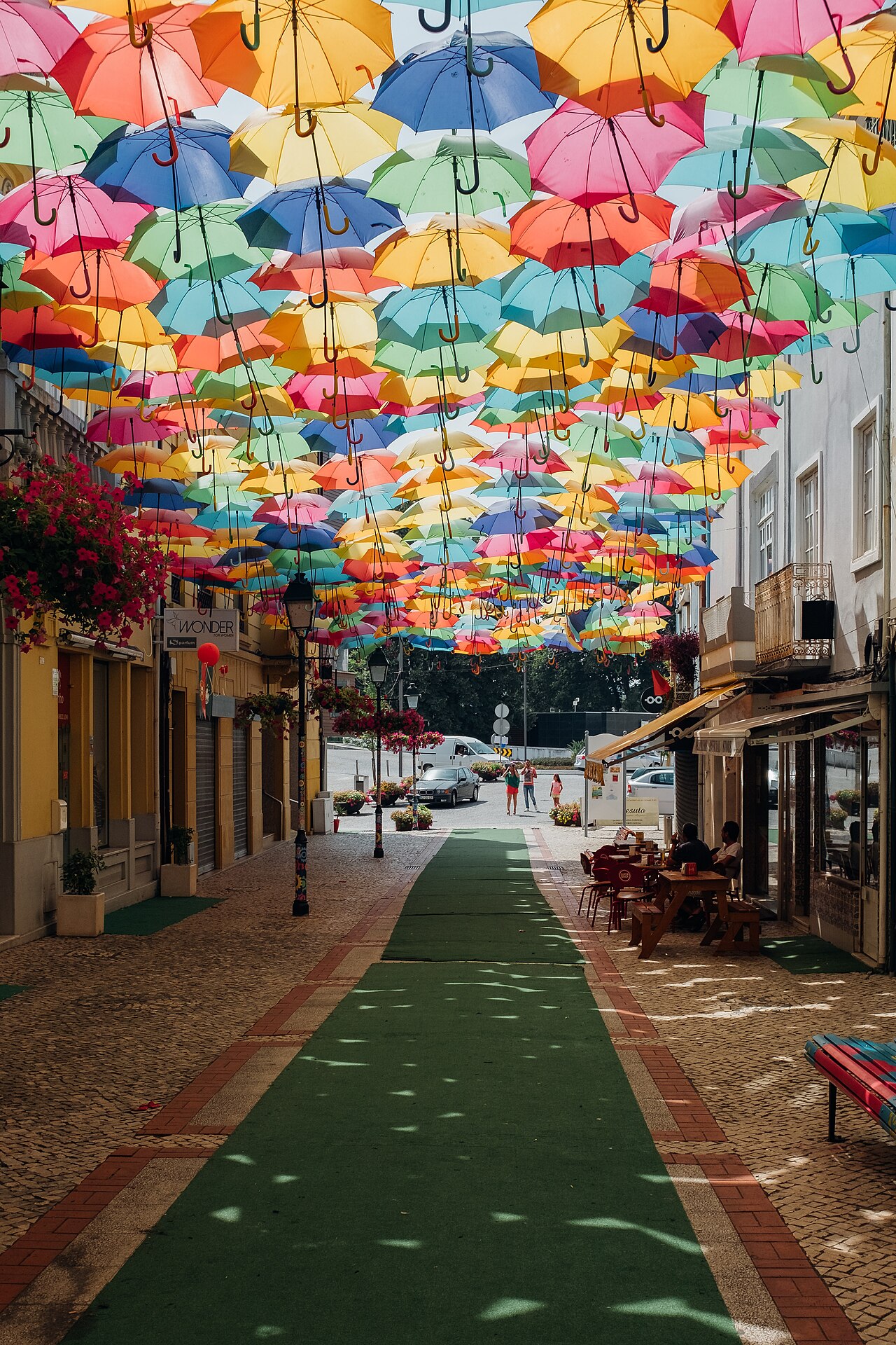 A long view down a Águeda street beneath the umbrella canopy, with dappled colored light falling across the green painted walkway and cobbles