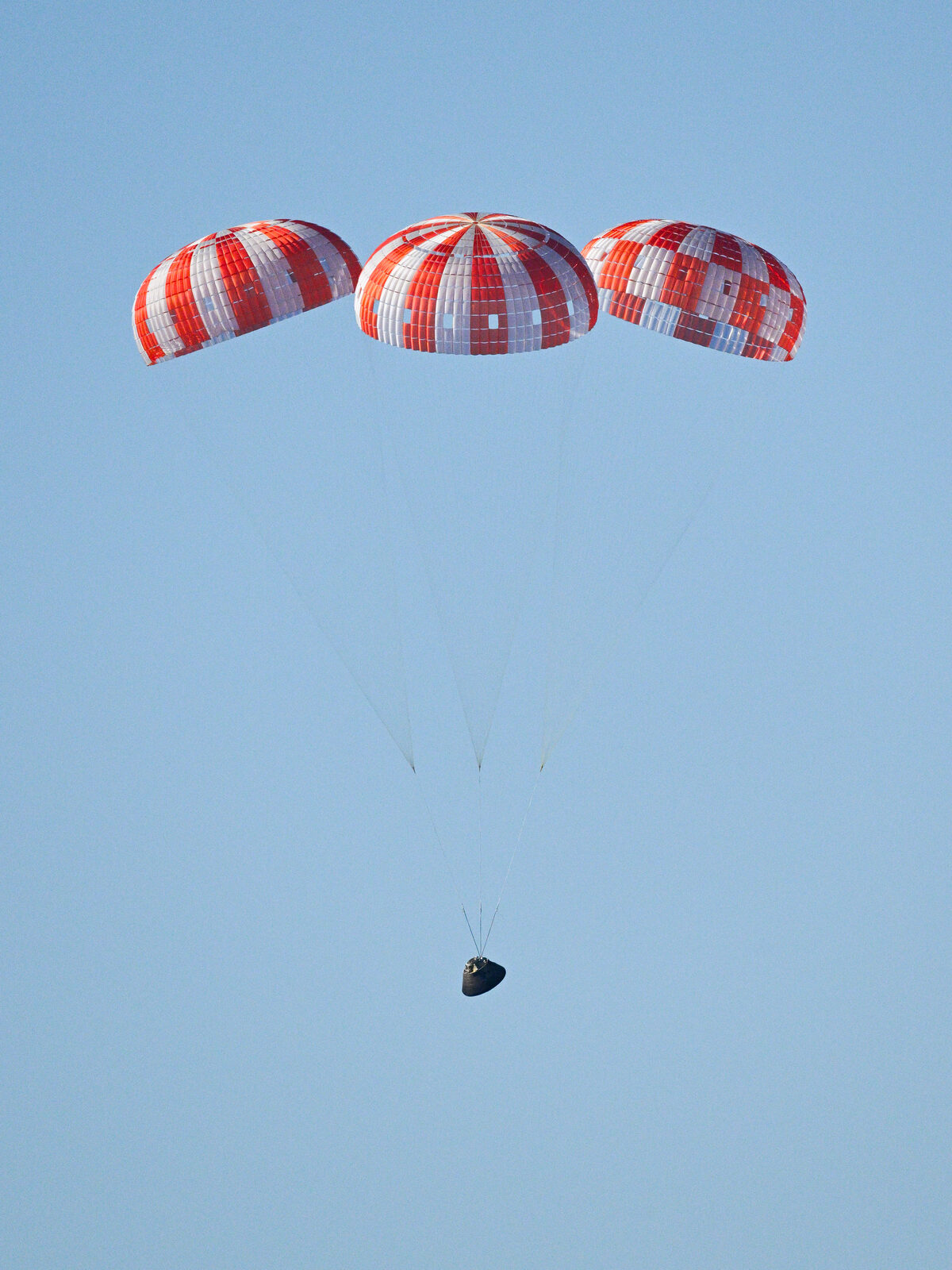 Orion's red-and-white parachutes deployed above the spacecraft as it descends toward the Pacific Ocean near San Diego