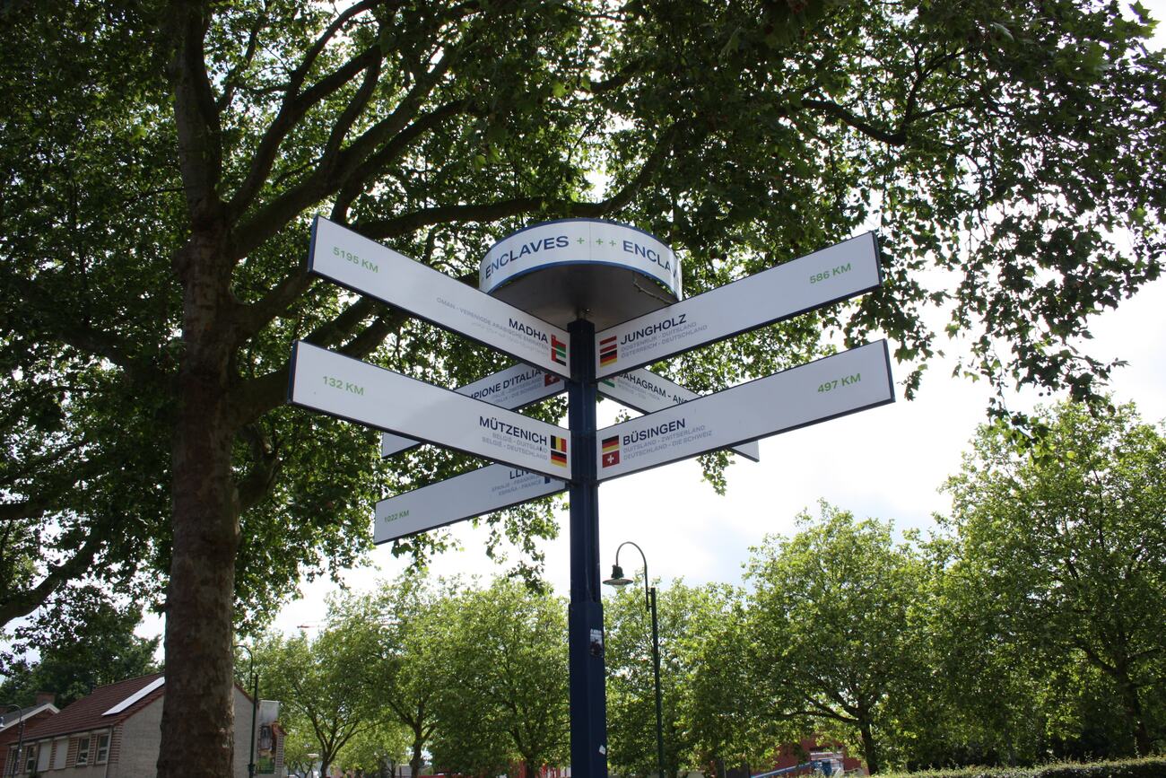 A fingerpost in Baarle with arms pointing toward other enclaves around the world, each labelled with a name, national flags and a distance in kilometres