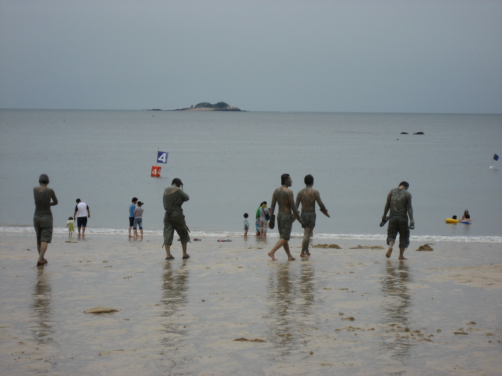 Festivalgoers coated head to toe in grey mud walking down the beach into the sea to rinse off