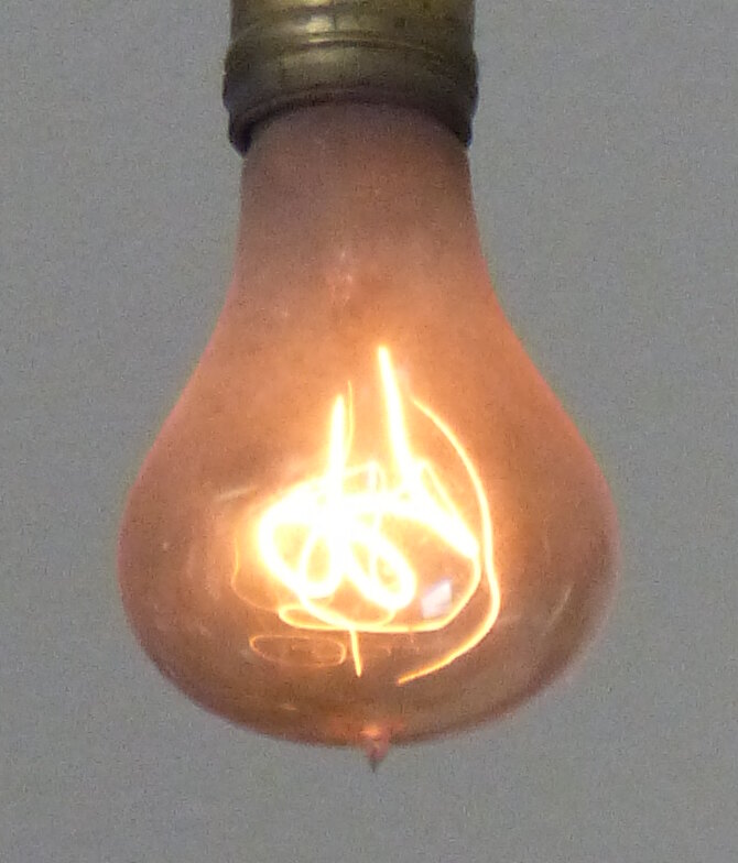 Extreme close-up of the Centennial Light showing its looped carbon filament glowing inside the glass