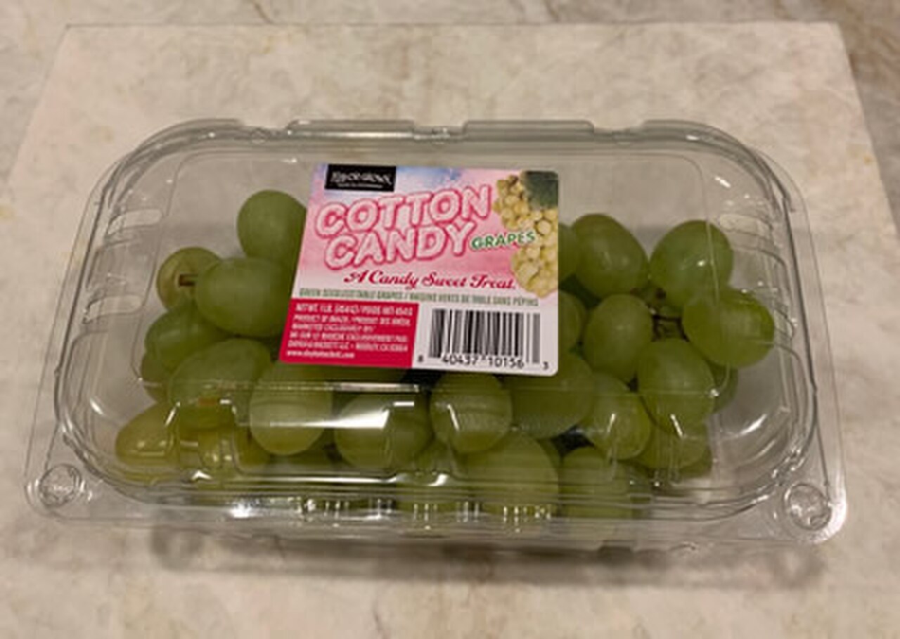 A bunch of pale green cotton-candy grapes held up in front of green leaves