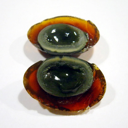 A century egg sliced open, showing a dark translucent amber-brown white and a creamy dark green-grey yolk