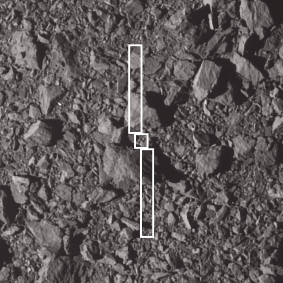 Close-up black and white view of an asteroid surface covered in angular boulders, with a thin white outline of the spacecraft's body and two long solar wings drawn over the rocks to show where it struck