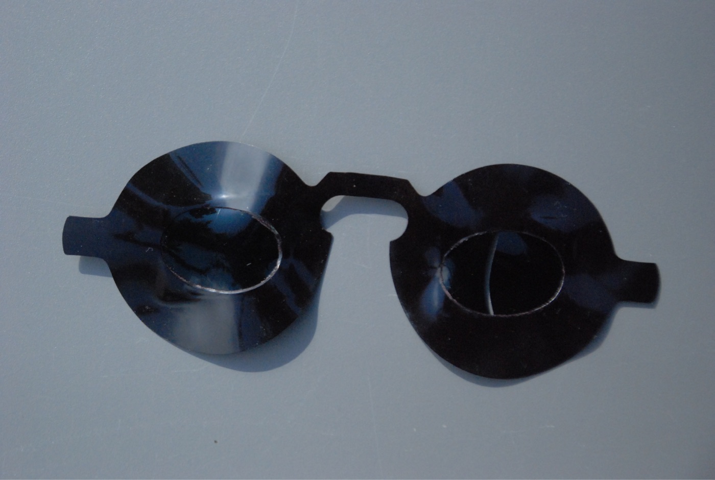 An antique eclipse viewer: two round discs of near-black moulded glass or lacquer joined by a bridge, each with a smaller oval lens set into the middle, with small side tabs