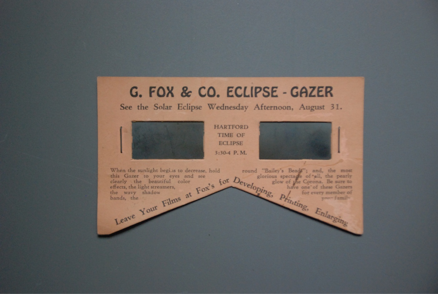 Pink cardboard eclipse viewer reading 'G. FOX & CO. ECLIPSE-GAZER — See the Solar Eclipse Wednesday Afternoon, August 31', with 'Hartford time of eclipse 3:30-4 P.M.' between the lenses