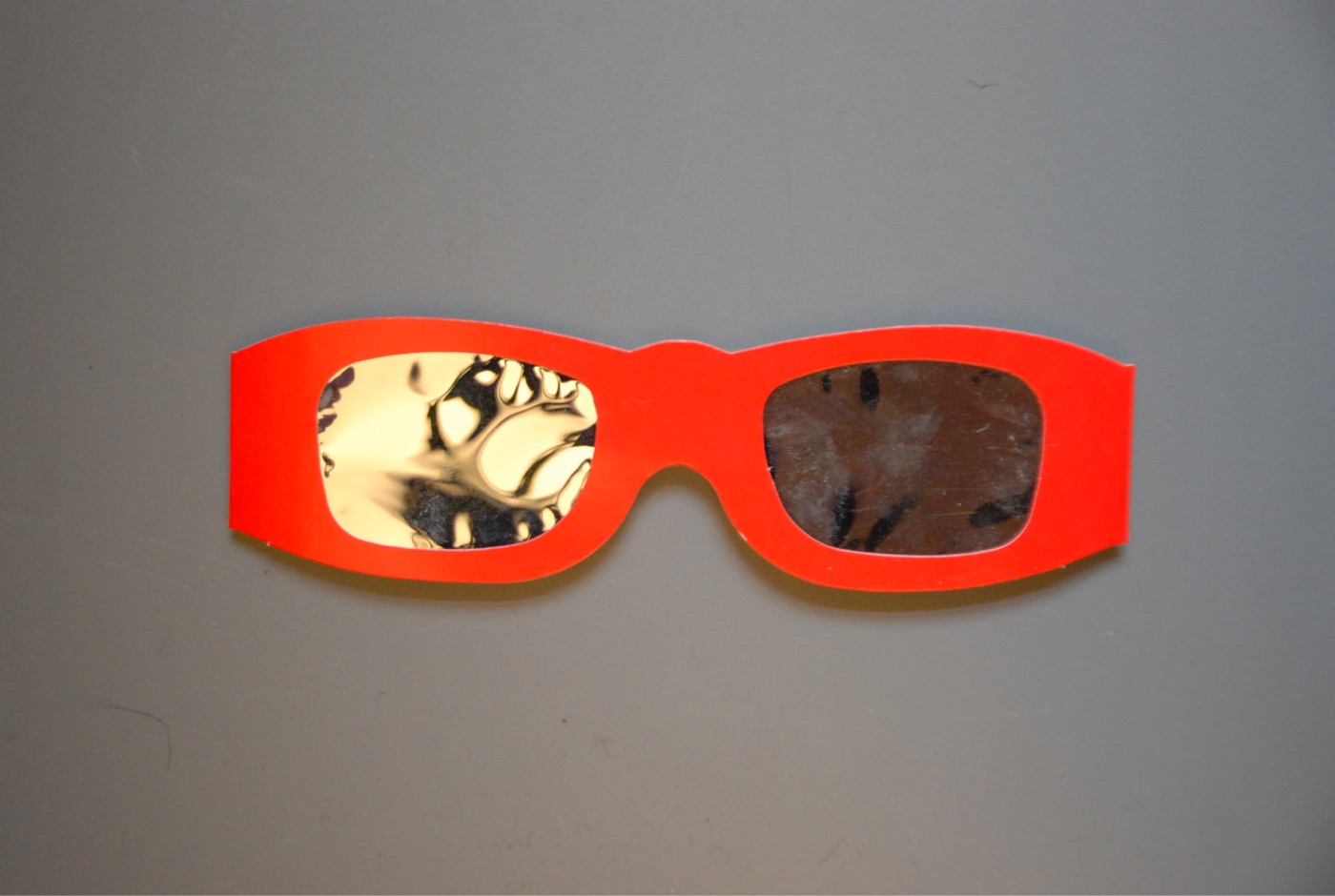 Bright red die-cut cardboard eclipse glasses with rectangular lenses of gold-toned reflective film