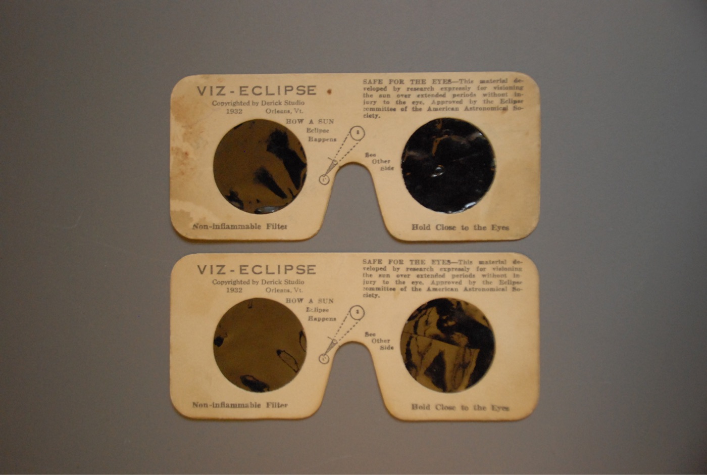Two cream-coloured 1932 eclipse viewers reading 'VIZ-ECLIPSE, Copyrighted by Derick Studio 1932, Orleans, Vt.', with round dark filters and a small diagram captioned 'How a Sun Eclipse Happens'