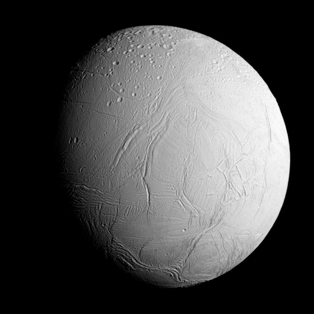 A close approach view of Enceladus, showing a heavily cratered northern half and a smoother, fractured southern region where the plumes originate