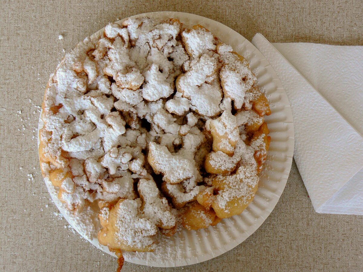 A funnel cake dusted with powdered sugar on a white paper plate