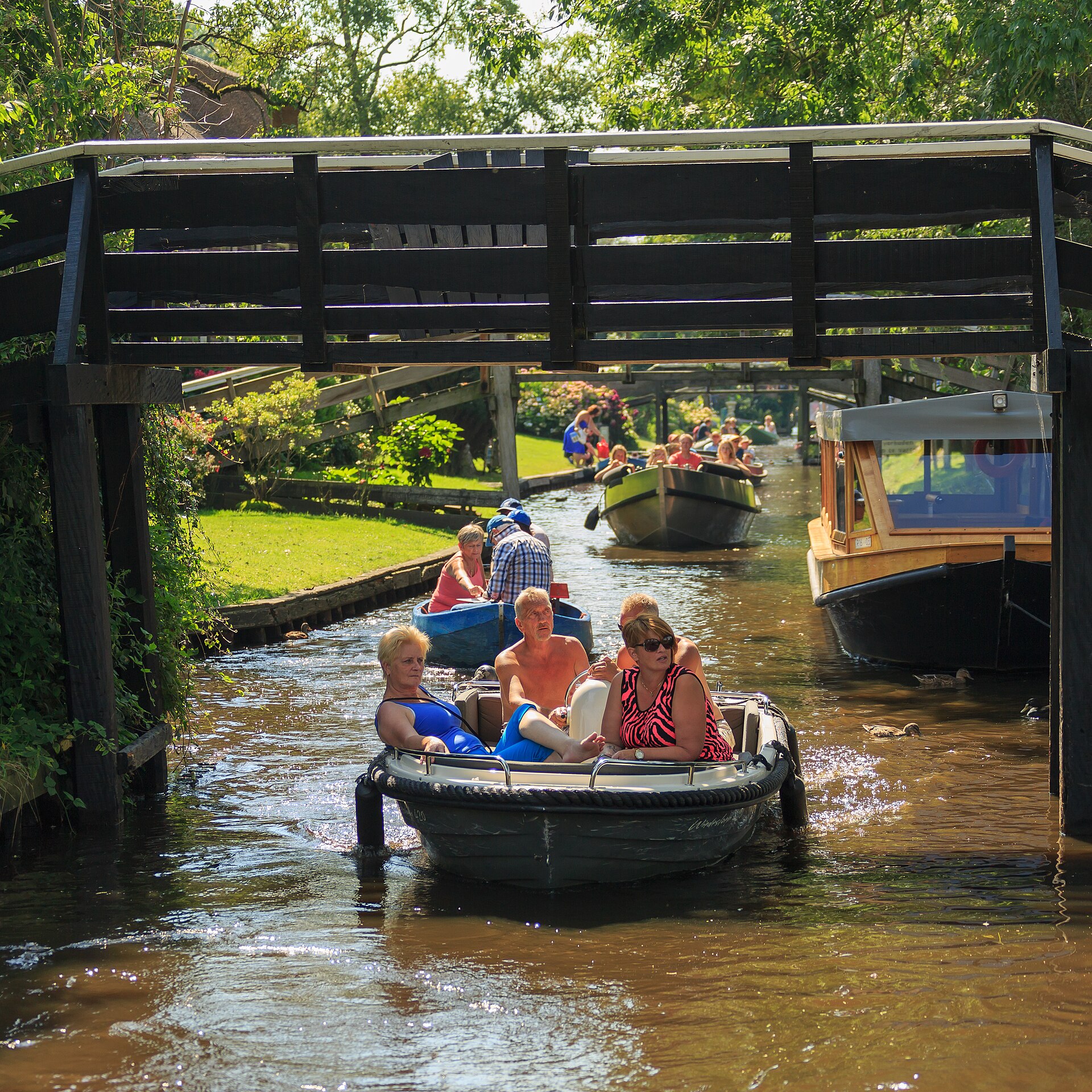 A small open boat gliding along a Giethoorn canal past thatched cottages and leafy gardens