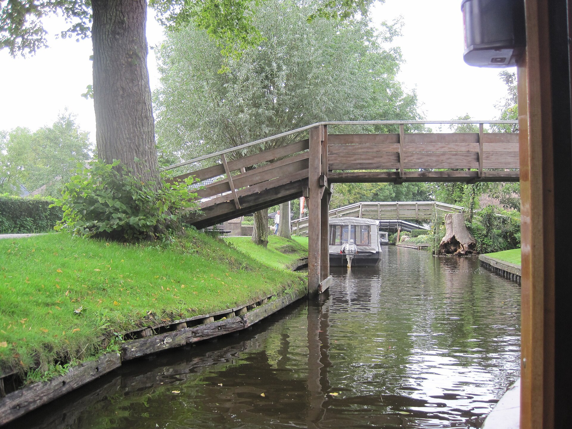 A steep arched wooden footbridge over a narrow Giethoorn canal, with greenery on both banks
