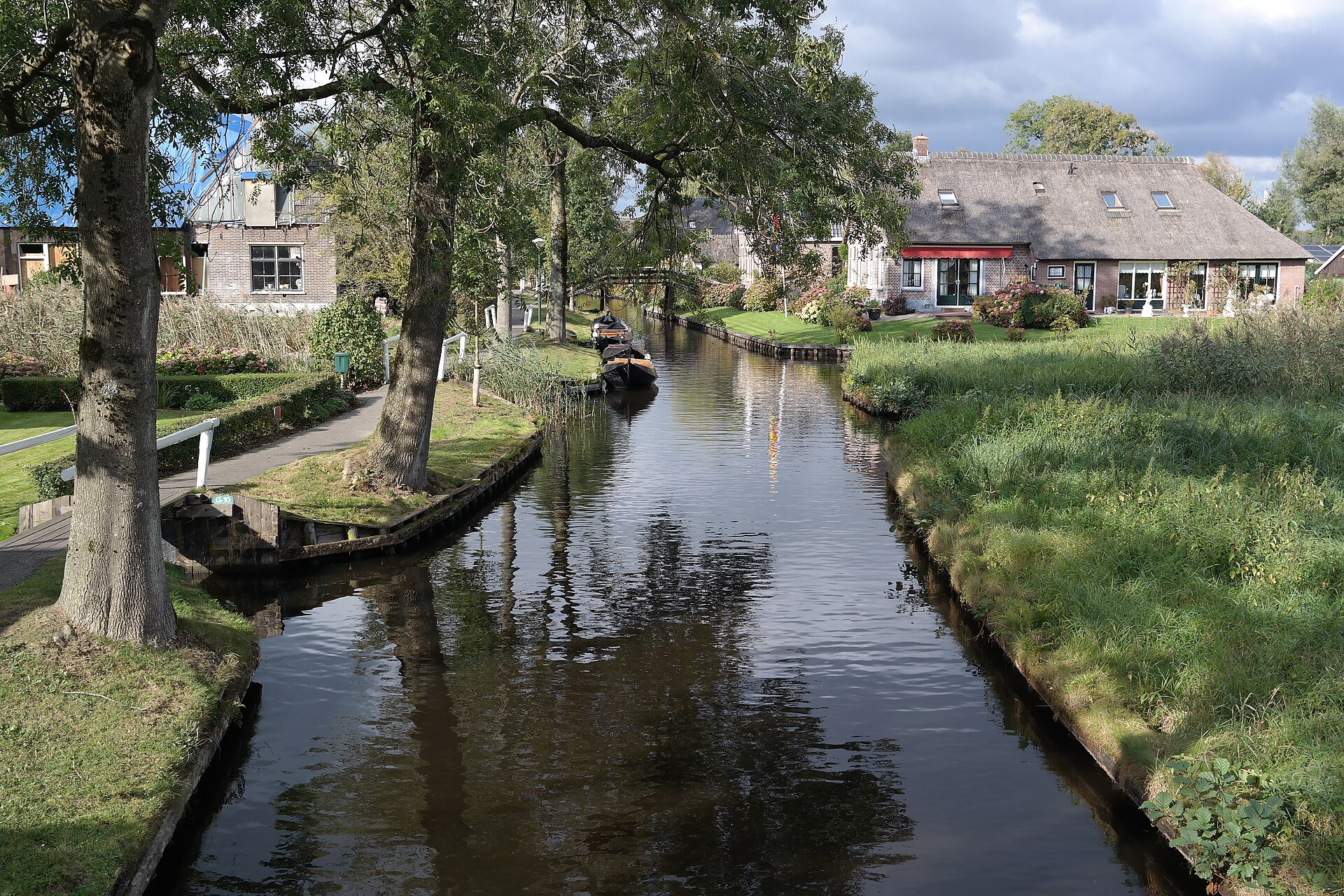 A calm Giethoorn canal at golden hour, cottages and trees mirrored perfectly in the still water