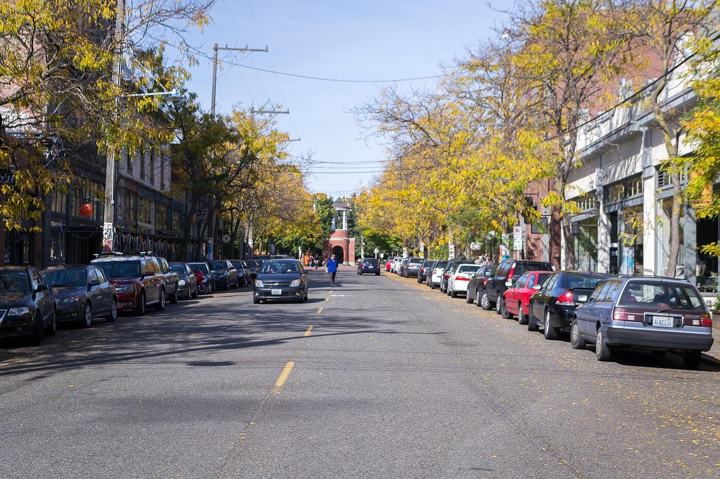 A tree-lined street in Ballard, Seattle, with brick storefronts, parked cars, and yellow autumn leaves