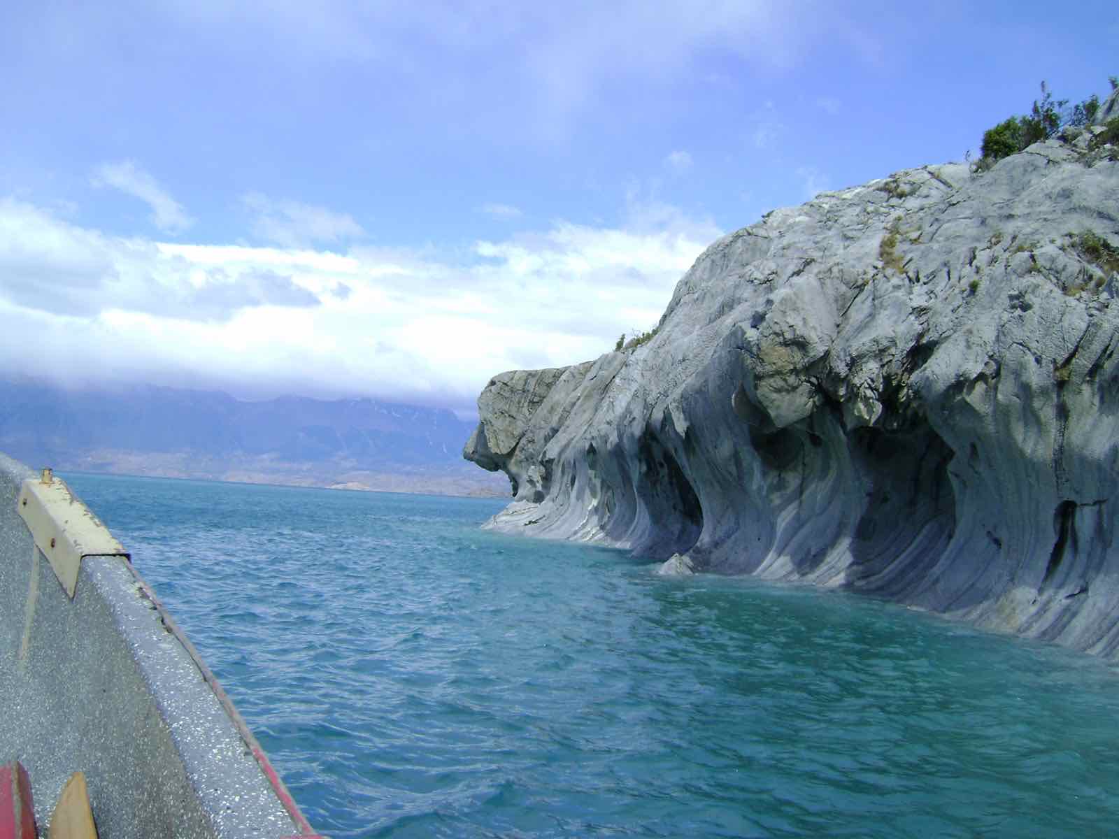 A small tour boat drifting beside the marble formations on the bright turquoise lake