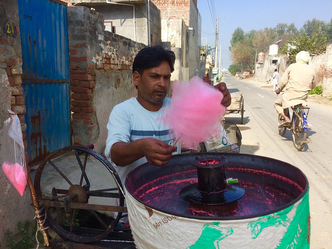 A vendor leaning over a spinning cotton candy machine, winding a paper cone through a web of fine sugar threads