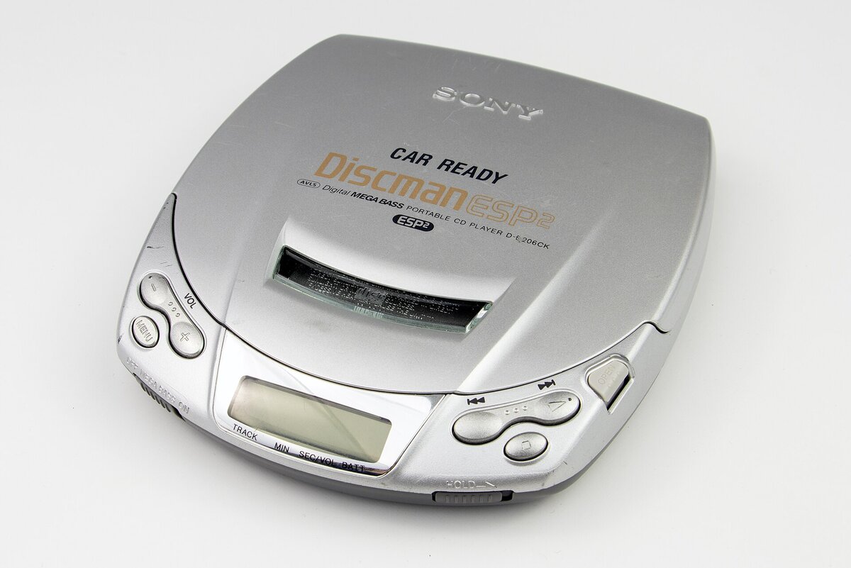 A closed silver portable CD player photographed on a plain white surface, with a small rectangular display, volume and skip buttons, and a hold switch on the front edge