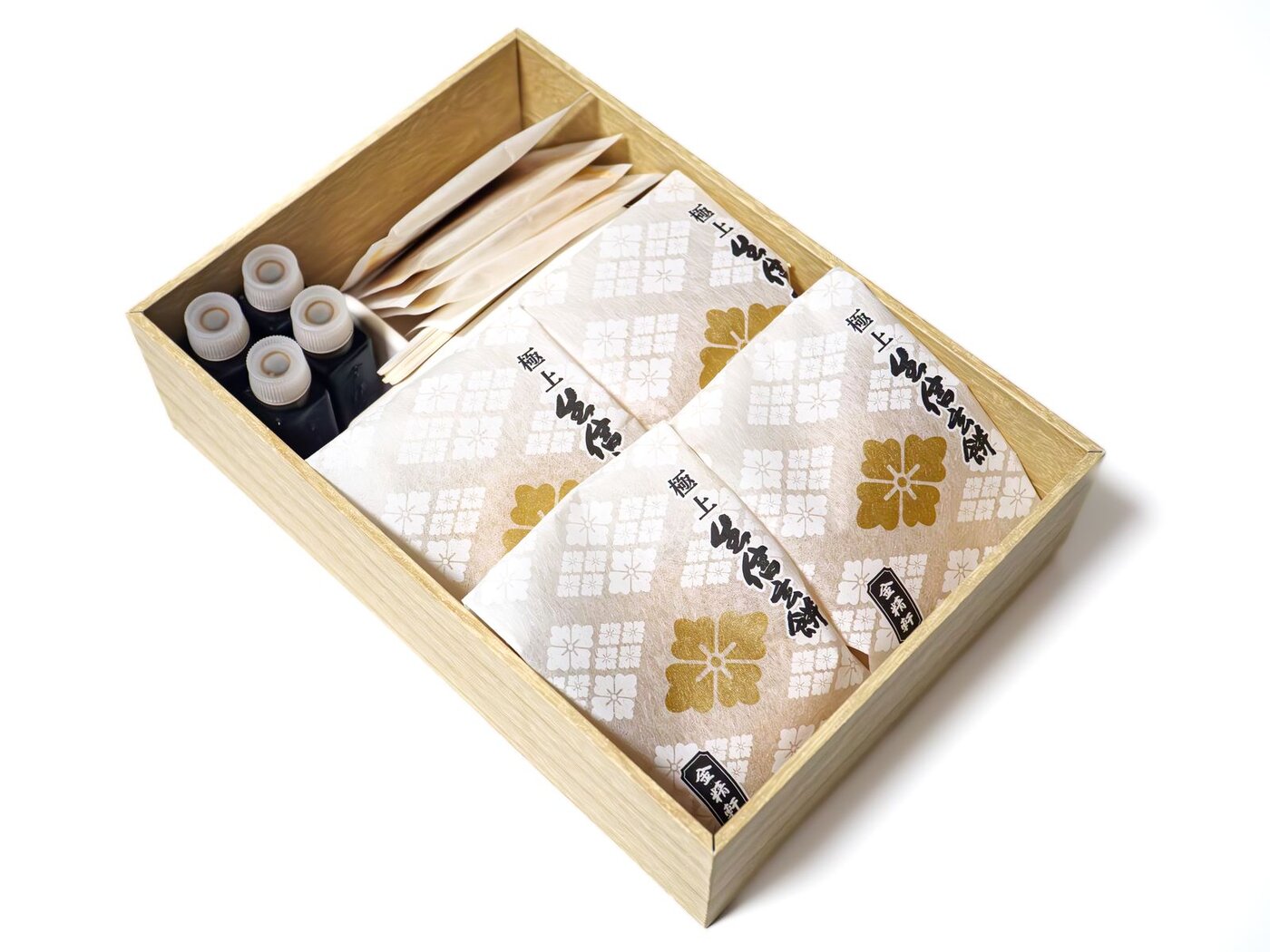 A wooden gift box holding three cloth-wrapped parcels of shingen mochi printed with gold flowers, alongside four small bottles of dark syrup and a row of wooden toothpicks