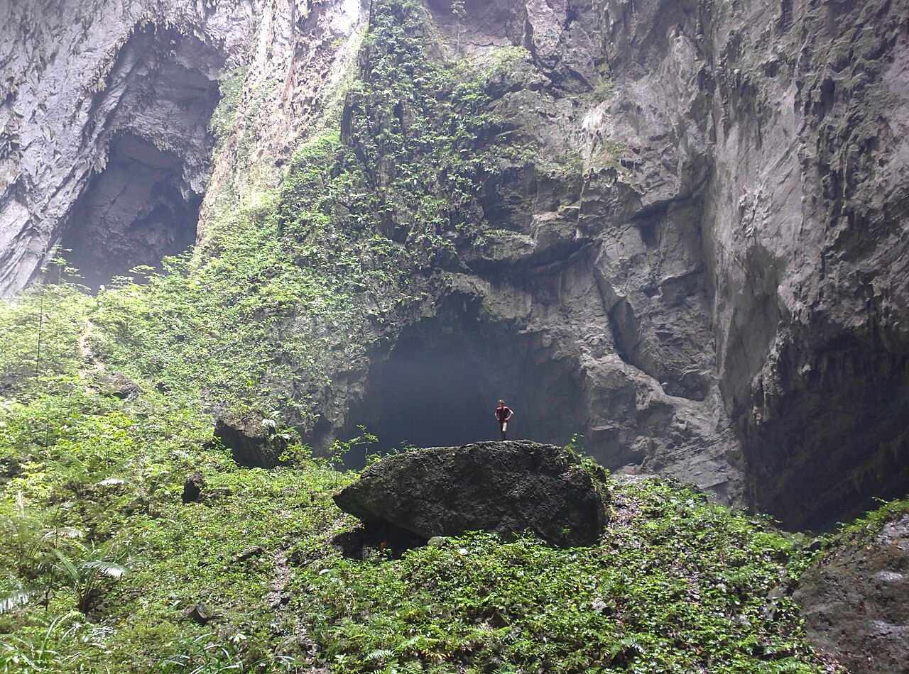 Light streaming into a vast Son Doong chamber with tiny human figures showing the enormous scale