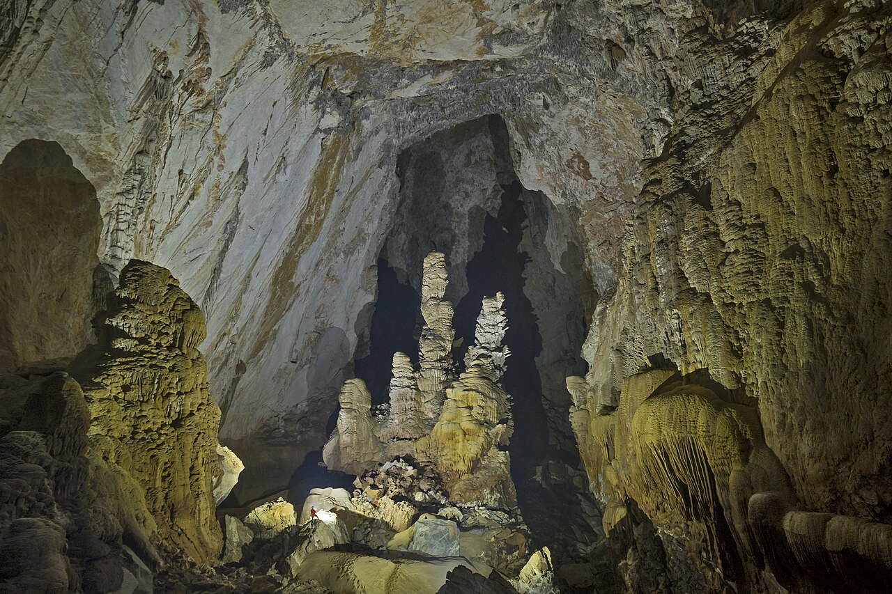 Enormous stalagmites towering over tiny explorers in the passage of Son Doong cave