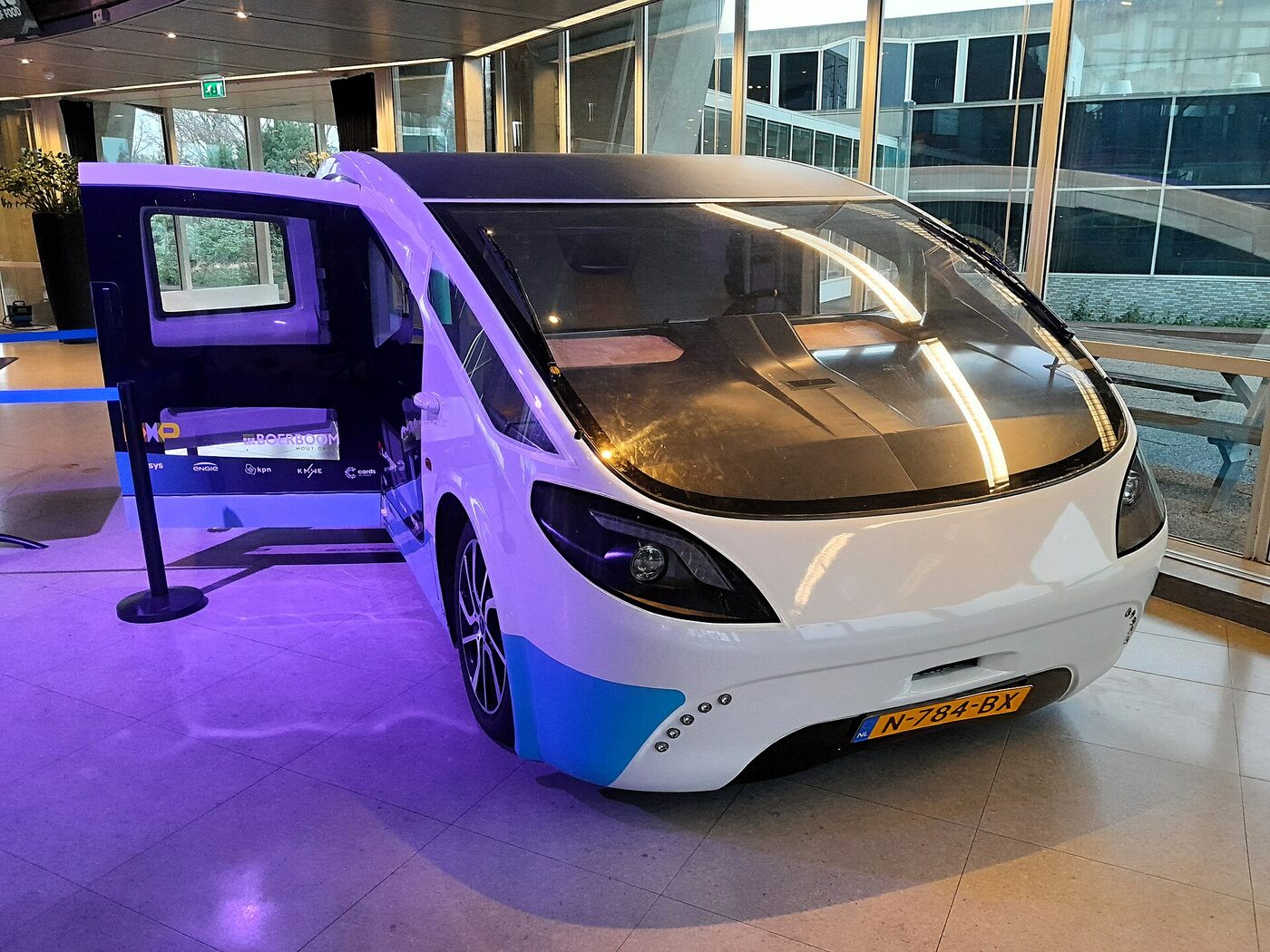 Stella Vita, a sleek white and blue solar campervan with a huge curved windscreen and a dark solar roof, parked indoors under purple lighting with its side door open