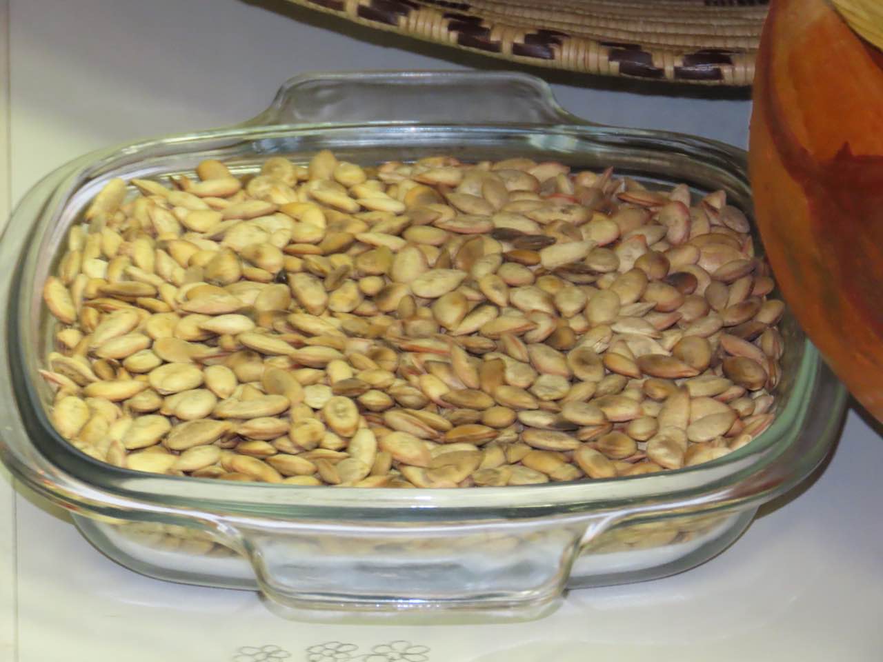 A glass dish heaped with roasted tsamma melon seeds, golden brown and flat, next to a woven basket