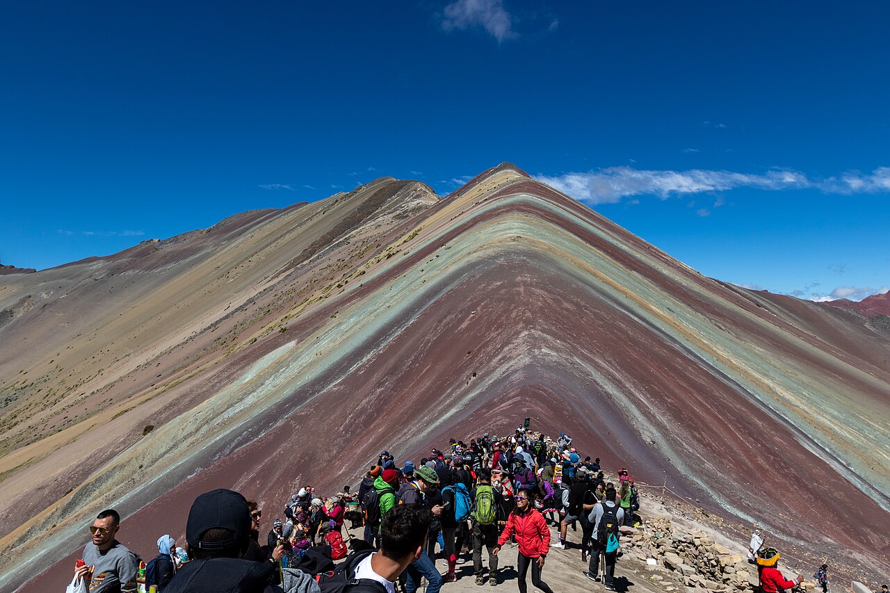 A line of hikers walking the ridge trail toward the colorful summit of Vinicunca