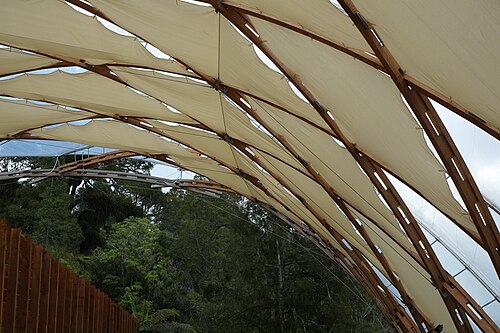 The modern woven timber canopy over the Waitomo cave entrance, framing the green hills